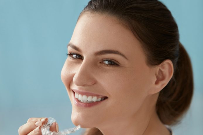 Dental care. Smiling woman with white smile using whitening tray. Portrait of girl with healthy teeth using invisible braces aligner, orthodontic silicone trainer for dental correction