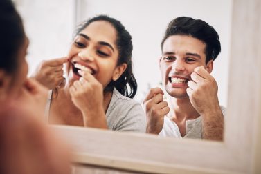 Young man and woman flossing in mirror smiling together