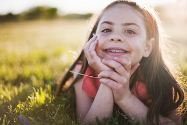 Young girl smiling with braces laying in grass