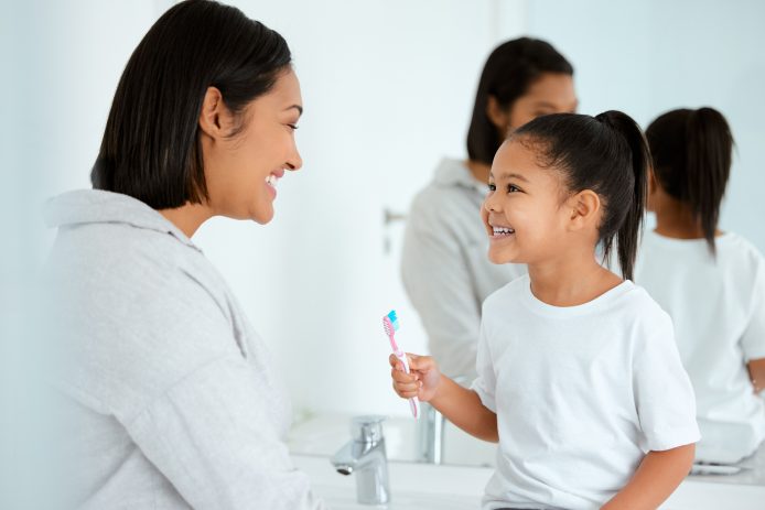 A mother and daughter smile while brushing teeth