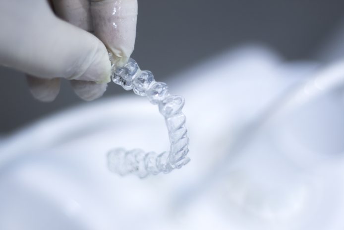 Hand with rubber glove holding clear aligners