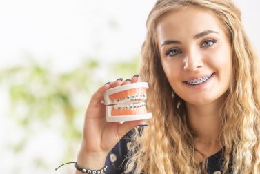 Teenage girl with braces holding up a model mouth with braces