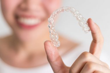 Smiling young woman holding up clear aligners
