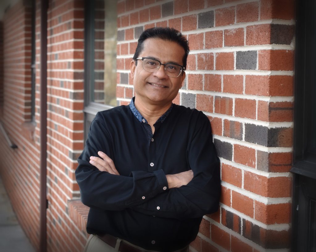 Dr. Sam Ghosh smiling against a brick wall