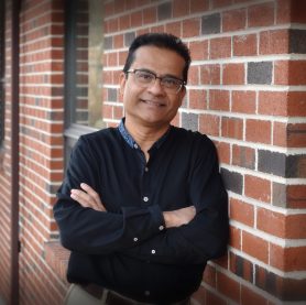 Dr. Sam Ghosh smiling against a brick wall