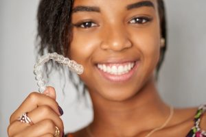 A teenage girl smiles while holding up Invisalign teen clear aligners